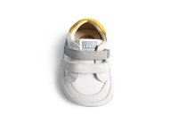 Sneaker in pelle bianca con cinturini in suede grigi, dettagli gialli, punta arrotondata e superficie testurizzata. Presenta un'etichetta di marca sulla linguetta.