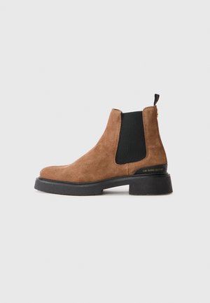 Brown suede Chelsea boot with black elastic side panel, black sole, and heel pull tab, shown against a plain light background.