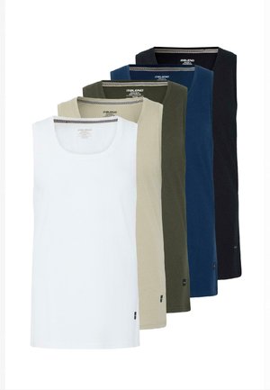 Jeune homme aux cheveux bouclés portant un débardeur beige, un short noir au genou, des chaussettes blanches et des baskets beiges, debout devant un fond clair.