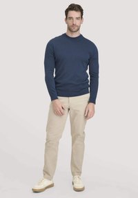 Marineblaues Sweater aus Strickstoff, runder Ausschnitt, taillierte Passform. Kombiniert mit beigen Hosen und weißen Schuhen mit strukturierten Sohlen.