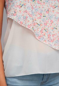 Blumenoberteil mit einem pastellfarbenen Druck, der pinke, blaue und grüne Blumen zeigt. Gestuftes Design aus weichem, leichtem Stoff mit einer durchsichtigen weißen Unterlage.