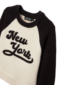 Pull noir et crème avec un col rond, présentant une texture duveteuse et "New York" brodé en écriture noire sur le devant.