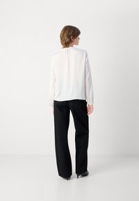 Hvid langærmet bluse med rynket halsudskæring, parret med sorte vide bukser med subtile glitrende detaljer og spidse sorte hæle.