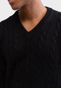 Czarny sweter z plecionki z dekoltem w kształcie litery V, charakteryzujący się teksturowanym wzorem i miękkim materiałem. Zbliżenie na obszar klatki piersiowej i szyi.