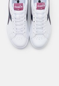 Vita sneakers med en slät lädertextur, med en rosa och grön logotyp samt mörkblå sidodetaljer. Snörningsdesign med perforerad tå.