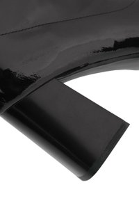 Botín de charol negro con tacón cuadrado grueso, textura suave y un diseño elegante. Detalle de costura a lo largo del borde superior.