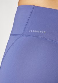 Visoke tajice od glatkog, svijetloplavog materijala s šivenim šavom i "CLOUDSPUN" logotipom u srebrnoj boji blizu struka.