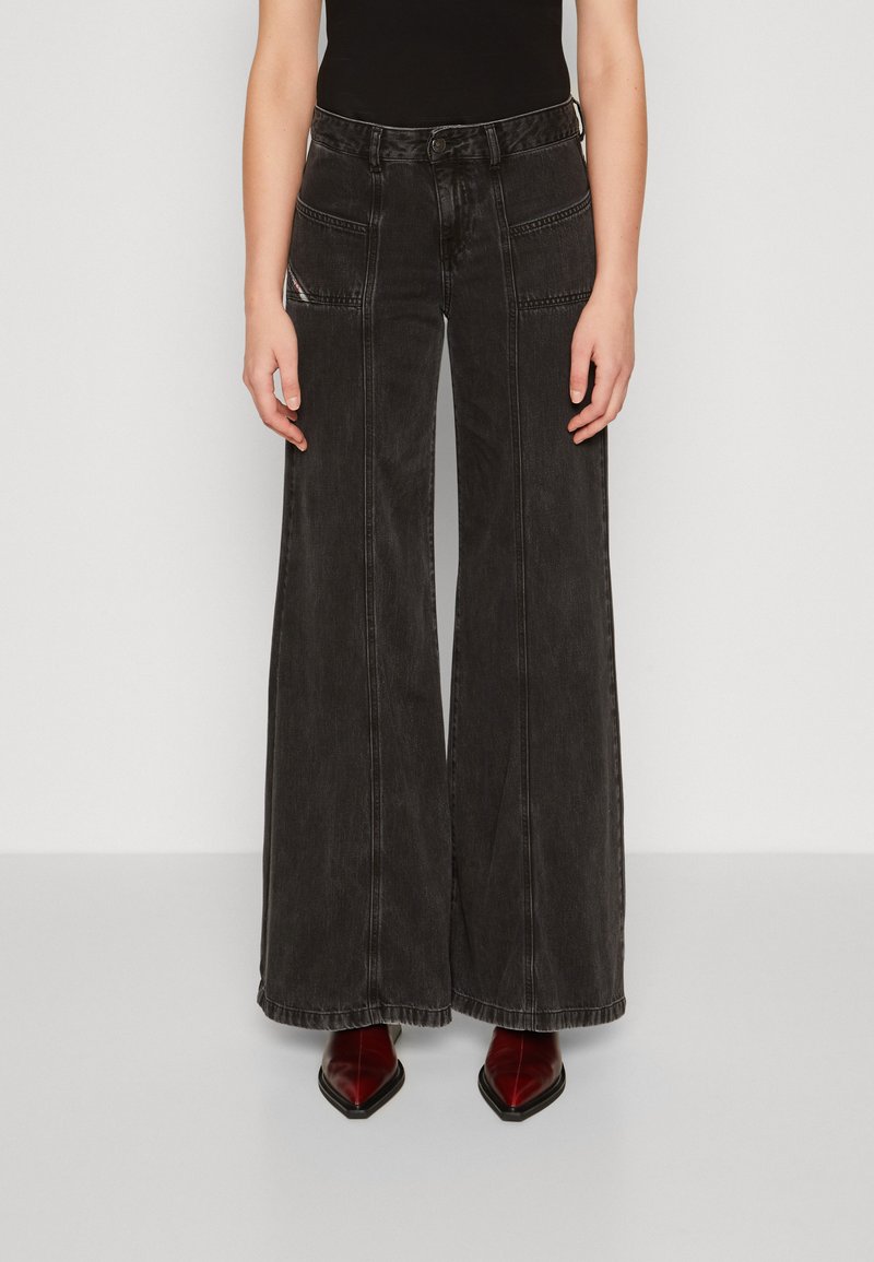 Schwarze denimweite Jeans mit hoher Taille, ausgestattet mit Fronttaschen und kontrastierenden Nähdetails. Kombiniert mit spitzen roten Knöchelstiefeln.