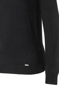 Czarny sweter zapinany na drutach z długimi rękawami, dopasowany krój i ściągacz u dołu. Mała metka z logo blisko brzegu jako detal.