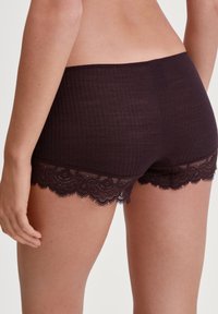 Donkerpaarse ondergoed met een geribbelde textuur, voorzien van een kantafwerking langs de benen. Het ontwerp heeft een gemiddelde taillehoogte en is gemaakt van een zachte, comfortabele stof.