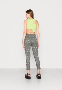 Top cropped verde com textura e costas recortadas, combinado com leggings pretas e brancas com padrão e pequenos detalhes amarelos. Sandálias de plataforma pretas.