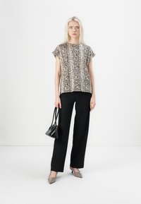 Short-sleeve blouse with a snake print pattern in beige and black, paired with black wide-leg trousers and gray pointed-toe heels.