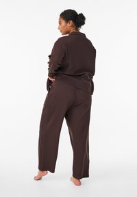 Brun loungewear-set som består av en långärmad topp och vida byxor, tillverkad av mjukt tyg med en avslappnad passform och minimala sömnadsdetaljer.