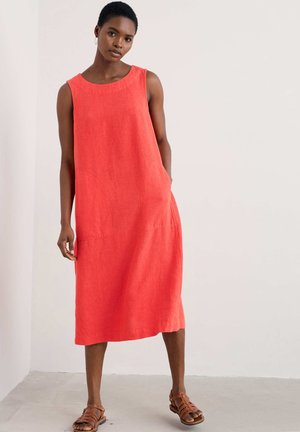 Coral linen sleeveless dress with a round neckline, side pockets, and a relaxed fit, styled with brown strappy sandals.