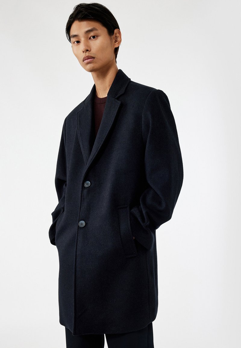 Marineblå uldfrakke med notched lapel, to knapper og sidelommer, der har en afslappet pasform og glat tekstur. Enkel design, ingen mønstre.