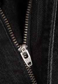 Primer plano de cierre de cremallera plateado YKK parcialmente abierto sobre tela de mezclilla negra.