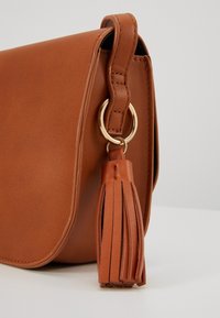 Brązowa skórzana torba na ramię z klapką, ozdobiona złotym pierścieniem oraz chwostem jako dodatkowym akcentem. Gładka faktura.
