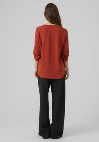 Maglia rossa a maniche lunghe realizzata in tessuto leggero, con scollo rotondo e vestibilità comoda, abbinata a pantaloni neri larghi.