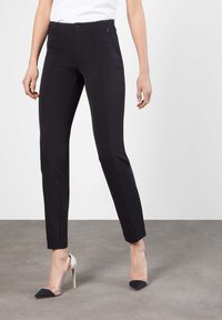 Pantalones negros ajustados con costuras sutiles, bolsillos delanteros con cremallera y una tela suave y elástica. Combinados con tacones puntiagudos en plata y negro.