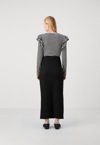 Črtasta dolga majica s ruffled rameni, kombinirana s črno rebrasto maksi krilo. Model nosi črne čevlje.