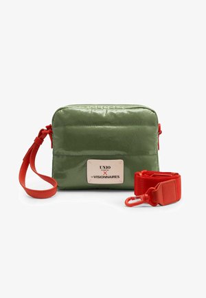 Piccola borsa rettangolare verde oliva con etichetta frontale e tracolla larga rossa rimovibile con fibbia in metallo su sfondo bianco.