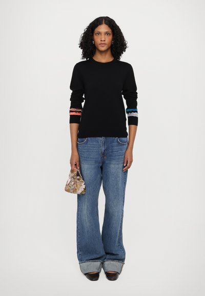 Svart strikket genser med fargerike stripede detaljer på ermene, kombinert med vide lyseblå denimjeans og en mønstrete minihåndveske.