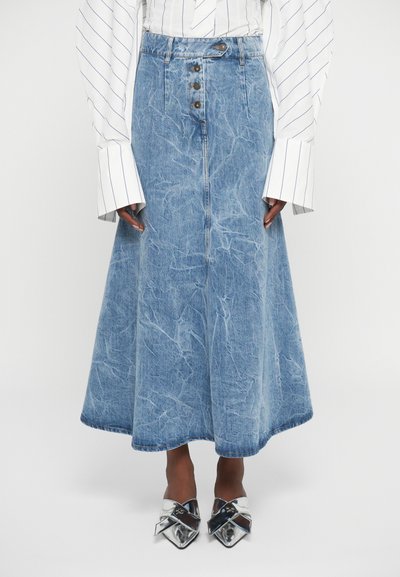 Denim midi rok met knopen aan de voorkant, gedragen met een witte shirt met lange mouwen met strepen en metallic puntige schoenen.