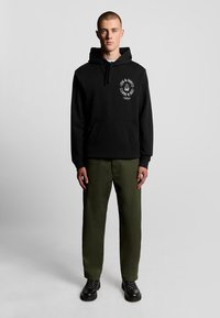 Felpa nera in cotone con tasca frontale e logo stampato bianco. Abbinata a pantaloni verde oliva e stivali neri con lacci.