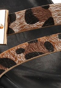 Tiras de sandalia de cuero con estampado de leopardo y hebilla rectangular dorada sobre una suela de textura negra.