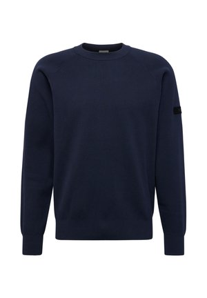 Granatowy, długi sweter z okrągłym dekoltem, z prążkowanymi mankietami, dołem i małą czarną naszywką na lewym górnym rękawie.