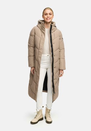 Long beige puffer coat with a hood, zip closure, and black accents. Features quilted texture and a straight fit, paired with white pants and beige boots.