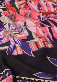 Multikleurige stof met grote bloemenpatronen in roze, paars en groen, tegen een zwarte achtergrond met geometrische accenten.