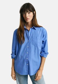 Lichtblauw button-up shirt met een zak, lange mouwen opgerold, gemaakt van katoen, met een afgeronde zoom en witte knopen.