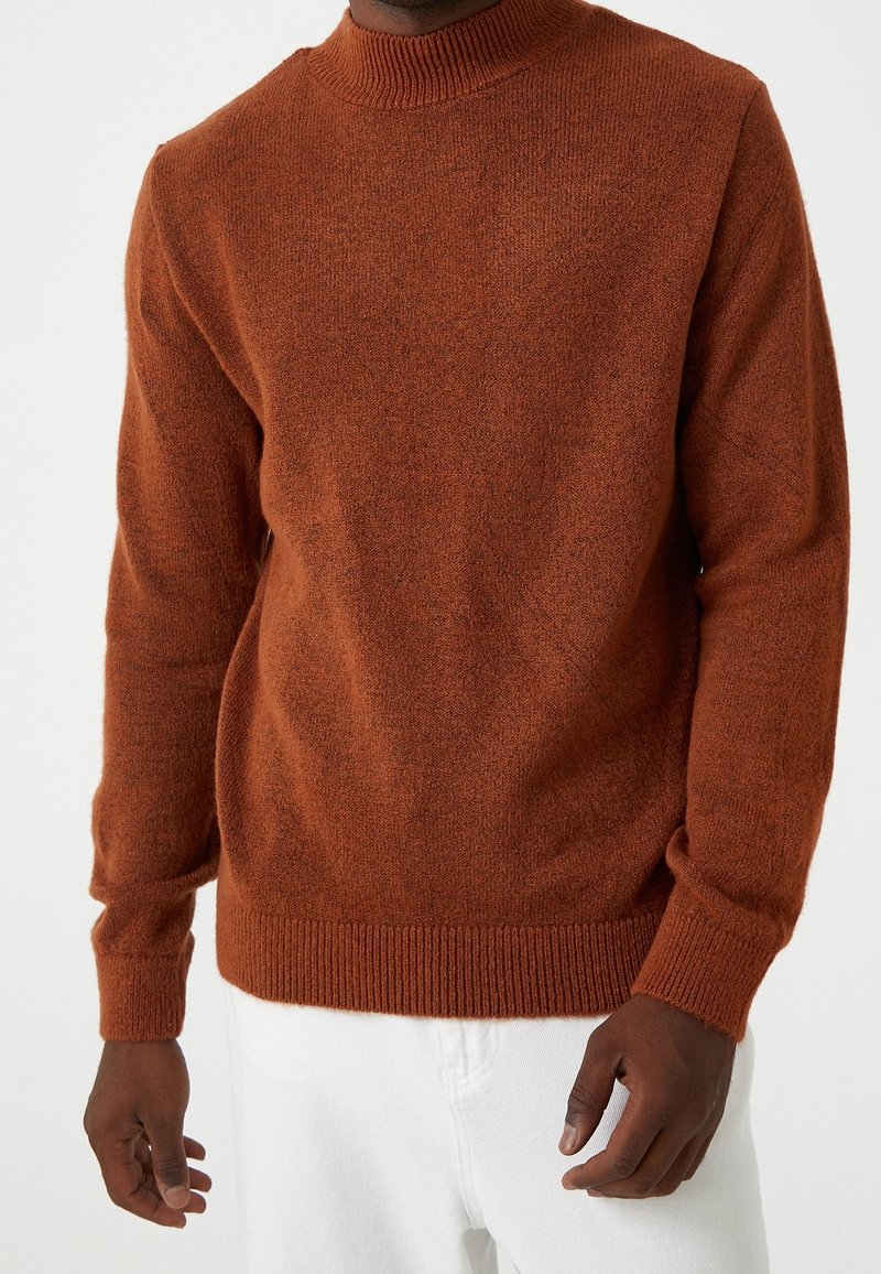 Suéter marrón de punto con cuello alto, mangas largas y puños acanalados, que presenta una textura suave y un ajuste holgado.