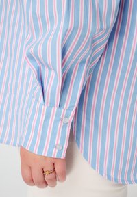 Chemise à rayures à manches longues en bleu clair, rose et blanc. Dispose de poignet boutonné et d'une coupe décontractée avec une texture de tissu douce et lisse.