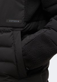 Veste matelassée noire avec des poignets en polaire texturée et une étiquette de la marque Icepeak sur la poitrine.