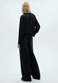 Blusa nera a maniche lunghe con un taglio morbido, abbinata a jeans neri a vita alta con gamba larga. Cuciture visibili e due tasche posteriori.