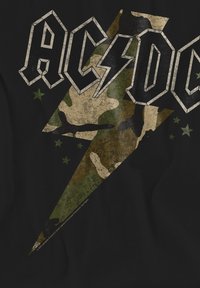 Schwarzes T-Shirt mit einem grün-braunen Camouflage-Blitzdesign, auf dem "AC/DC" in abgenutzten weißen Buchstaben und grünen Sternakzenten zu sehen ist.