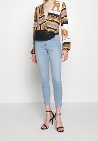 Camiseta de manga larga con un atrevido estampado de animal en negro, blanco y dorado; combinada con unos jeans ajustados azul claro y tacones negros con tiras. Bolso de cintura negro.