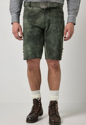 Man draagt donkergroene traditionele leren korte broek met een decoratieve riem, witte sokken, bruine veterlaarzen en een geruit overhemd.