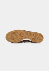 Suola di sneaker in gomma marrone con modelli di trazione circolari e accenti bianchi. Presenta un design testurizzato e una suola di un marrone chiaro.