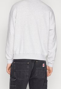 Sweatshirt à col rond gris clair avec des poignets et un ourlet côtelés. Porté avec un pantalon cargo noir doté de poches arrière et d'une étiquette de logo. Design minimaliste.