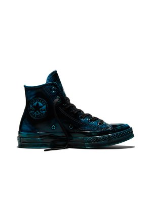Zwarte hoge Converse sneaker met zichtbare veters en logo-patch op een witte achtergrond, gezien van opzij.
