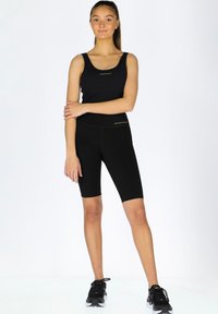 Svart atletisk linne och högmidjade shorts med en mjuk textur. Båda har en minimalistisk design och diskret logotypdetalj.