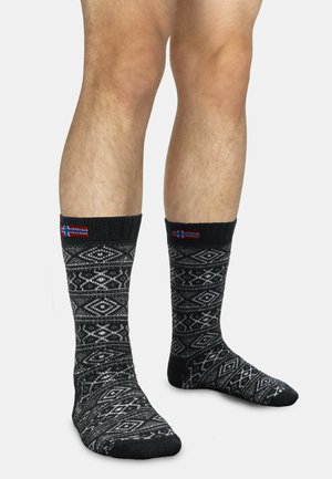 Schwarze Socken mit weißen geometrischen Mustern, gerippten Bündchen und kleinen Flaggenakzenten. Hergestellt aus einem weichen, strukturierten Stoff.