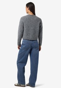 Grauer Strickpullover mit rundem Ausschnitt, kombiniert mit lockeren blauen Jeans. Der Pullover hat eine weiche Textur und ein kurzes Design.