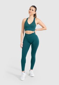 Teal geribbelde sportbeha met een V-hals en uitsnijdingen, gecombineerd met hooggetailleerde, gestructureerde legging. Draag met witte sportschoenen.