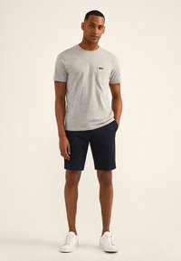 Grijze katoenen t-shirt met een borstzak, gecombineerd met marineblauwe shorts. Model draagt witte sneakers. Eenvoudig, casual ontwerp met een losse pasvorm.