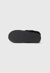 Sort sål af slippers med et gentaget præg af "BIANCO" logo-mønster, fuzzy øvre kant synlig, isoleret på en hvid baggrund.