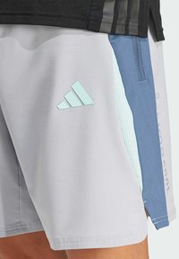 Shorts de sport gris et bleu avec un tissu texturé, présentant un logo à trois rayures bleu clair et une poche latérale avec des perforations.